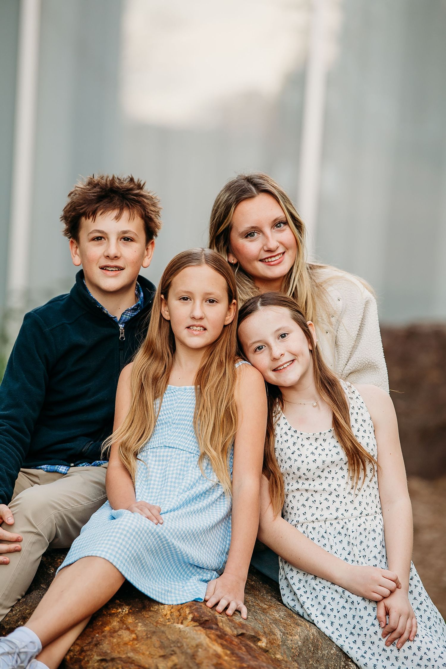 A mother and three children sit together on a log outdoors.