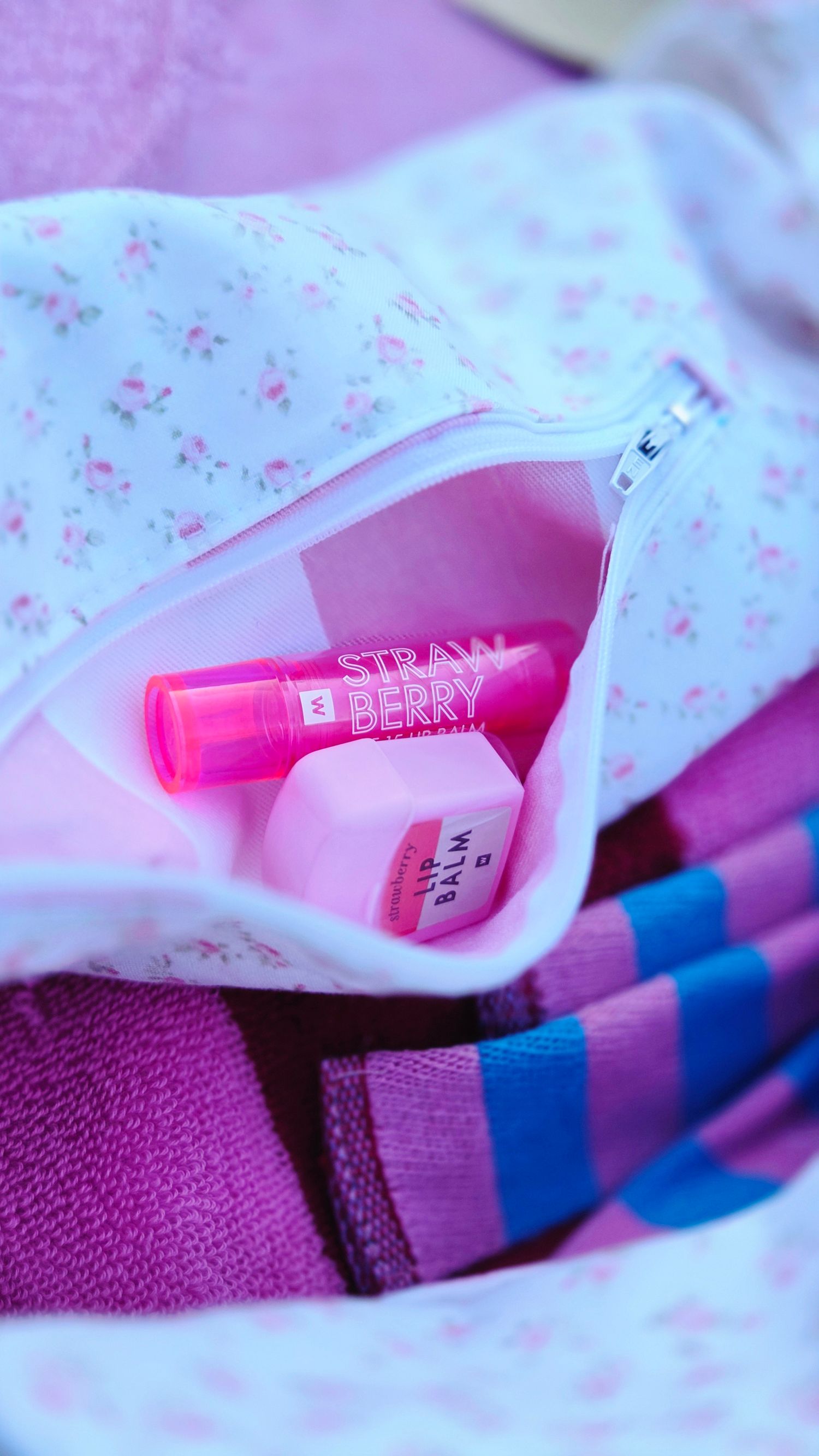 Pink floral cosmetic bag with strawberry lip balm and pink beauty products inside.