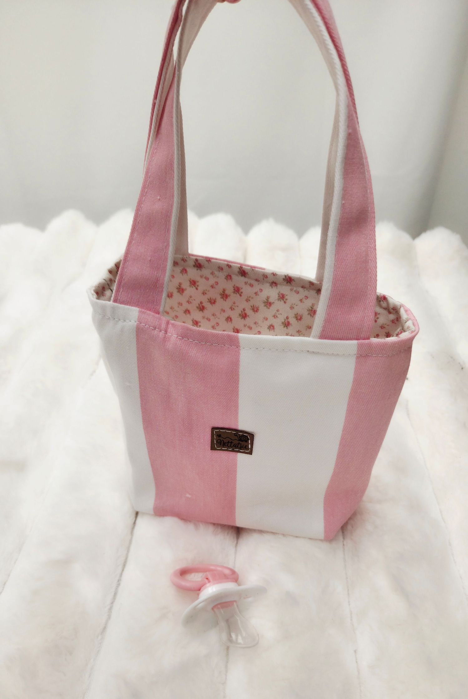 Pink and white striped fabric tote bag with floral lining and leather label, displayed on white surface.