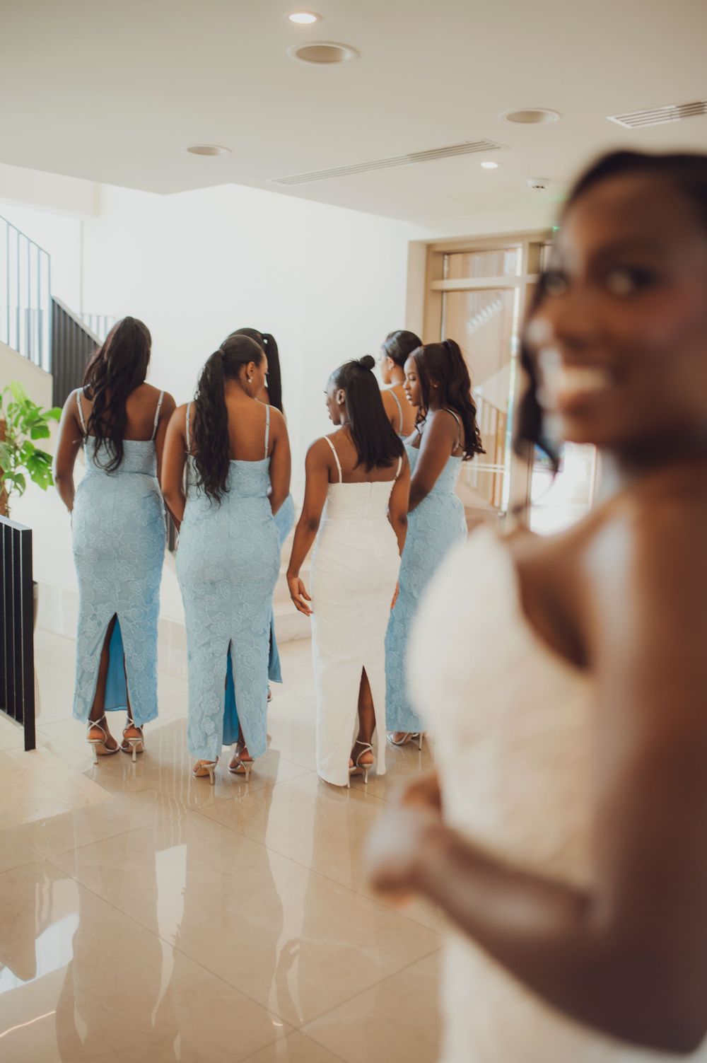 Bride in white gown with bridesmaids in light blue dresses walking through elegant venue hallway.