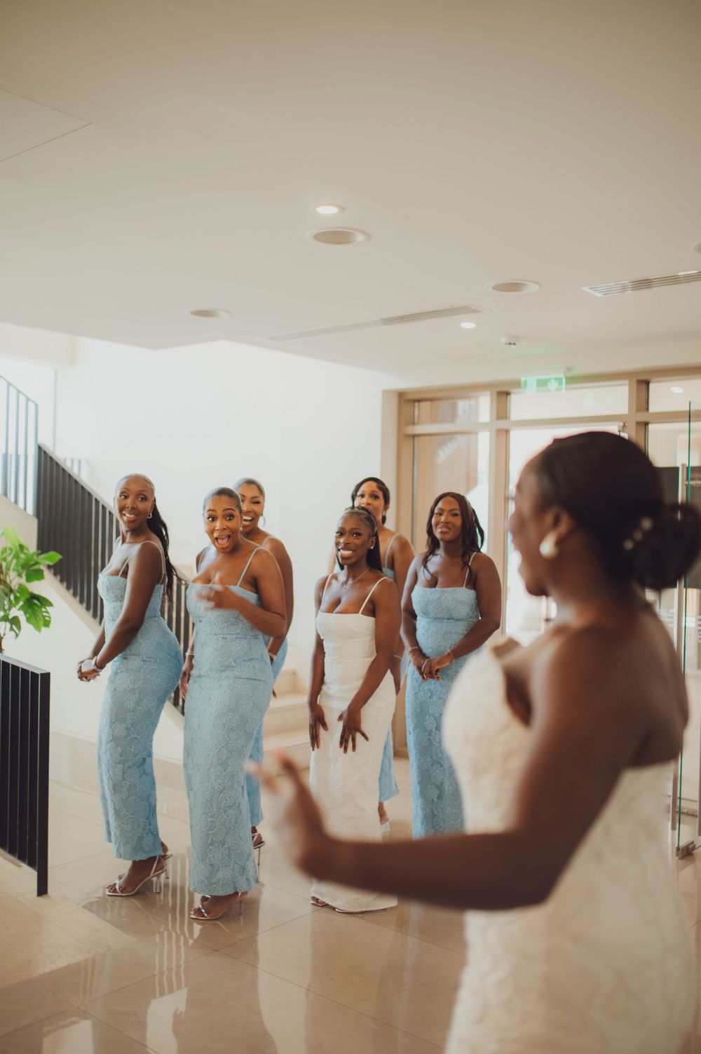 Bride in white gown reveals look to bridesmaids in light blue dresses during wedding day first look moment.