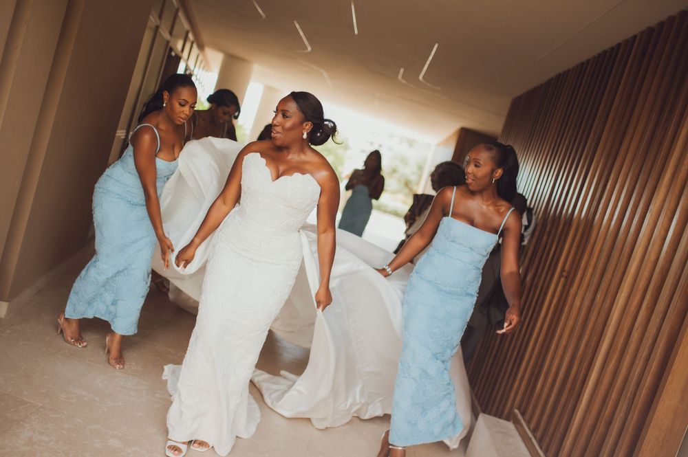 Bride in white gown walks with bridesmaids in light blue dresses through a modern venue hallway.
