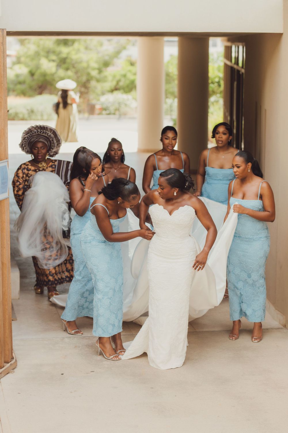 Bride in white gown surrounded by bridesmaids in light blue dresses being helped before wedding ceremony.