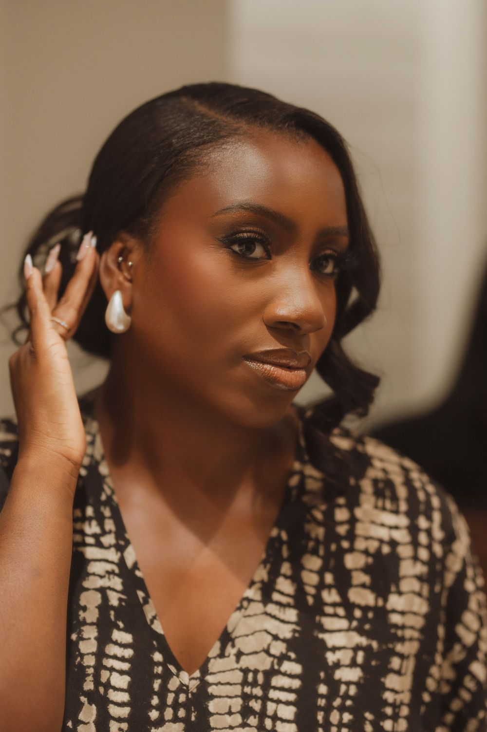 A young Black woman with pearl earrings and dark hair poses thoughtfully in a patterned black and white top.