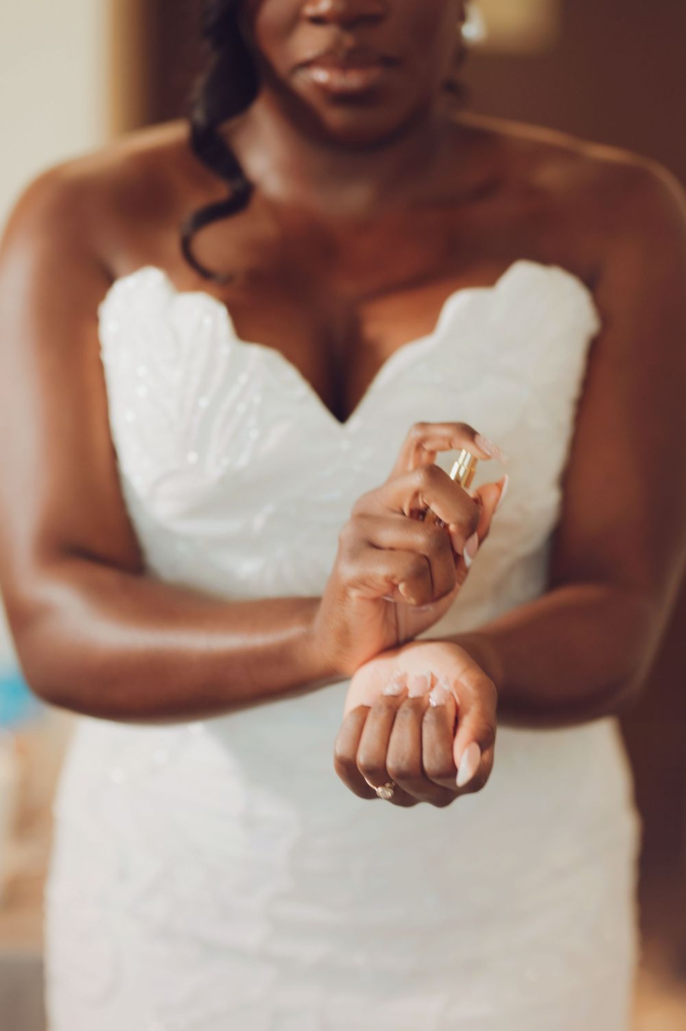 A Black bride in a white strapless scalloped wedding gown sprays perfume on her wrist while getting ready.