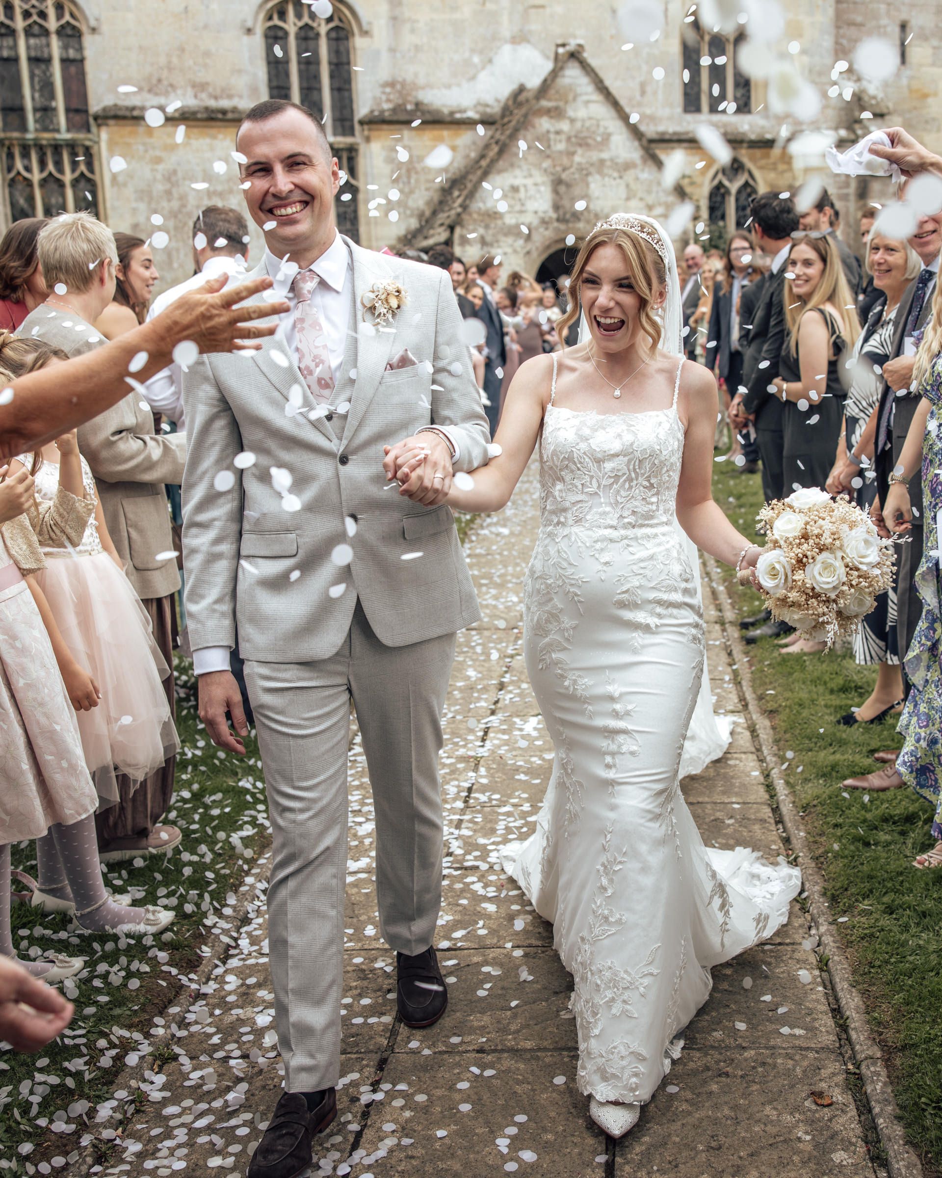 Shauna and Mark laughing beneath white confetti outside St Michael and All Angels Church
