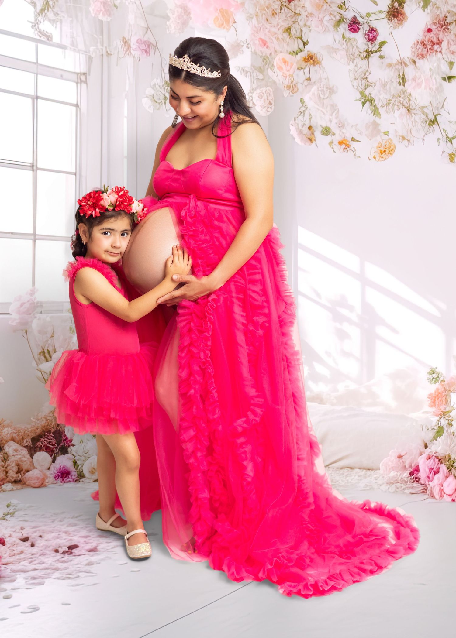 Pregnant woman and young girl in matching hot pink tulle dresses pose together in floral studio maternity shoot.