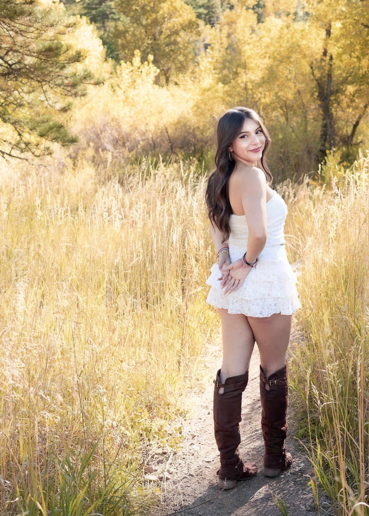 Young woman in white top, lace shorts, and brown knee-high boots poses on a dirt path surrounded by tall golden grass.