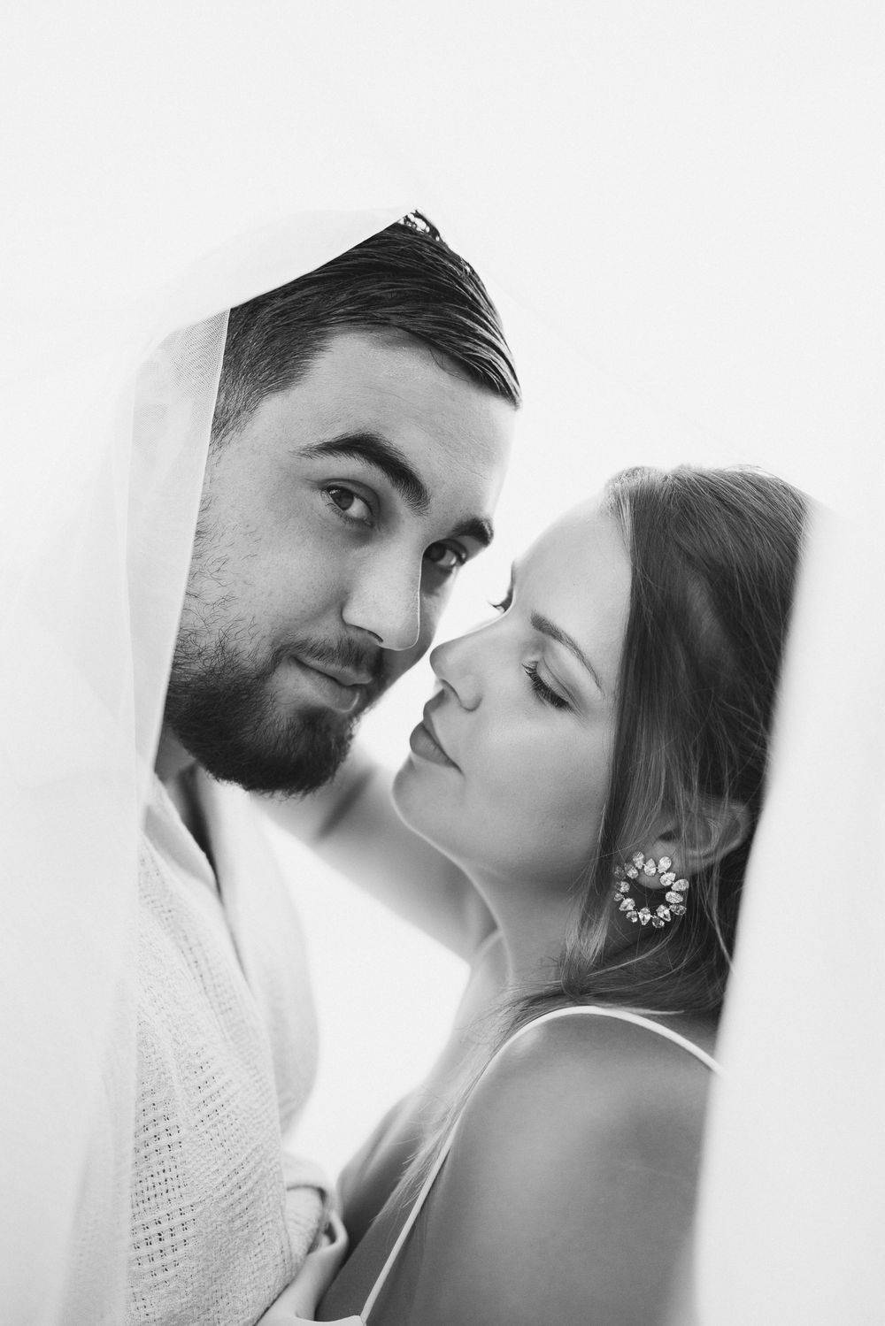 Black and white portrait of bride and groom sharing intimate moment under veil.