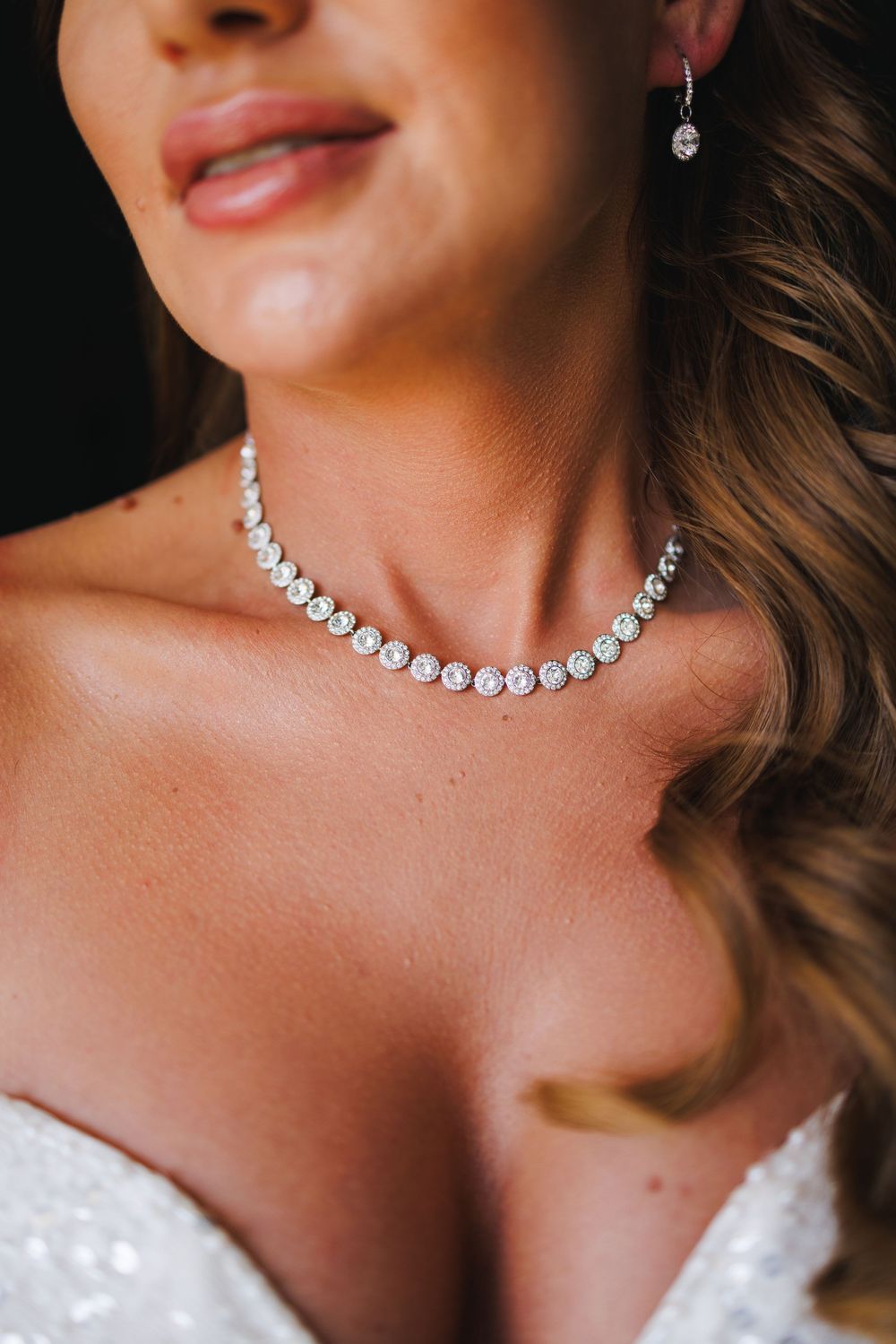 Bride wearing a sparkling diamond tennis necklace and drop earrings with a strapless white wedding gown.