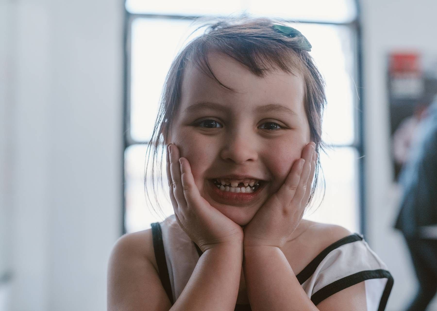 Happy young girl smiling with hands on cheeks, showing missing teeth in a candid portrait photo.