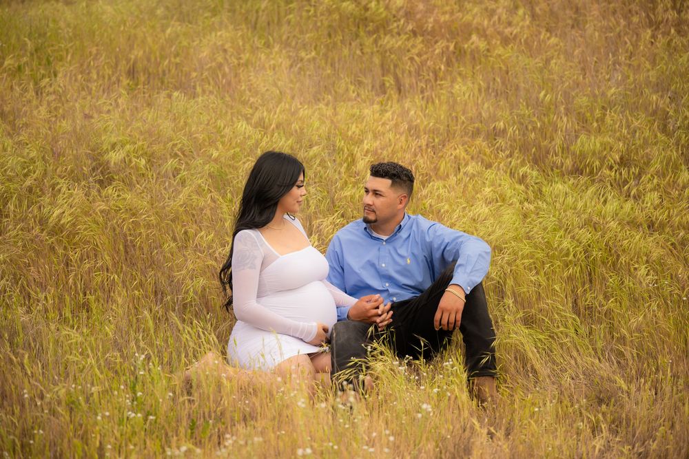 Expectant couple sitting together in a golden grassy field during an outdoor maternity photography session.