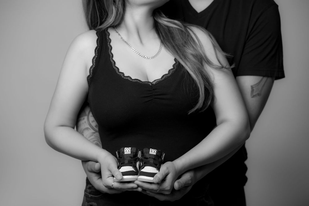 Black-and-white maternity portrait of an expectant couple holding ultrasound pictures in front of the mother's baby bump.