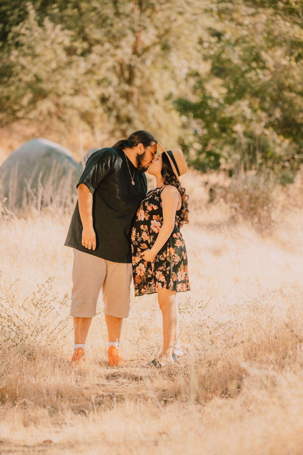 Couple sharing a romantic kiss in a sunlit field surrounded by golden grass.