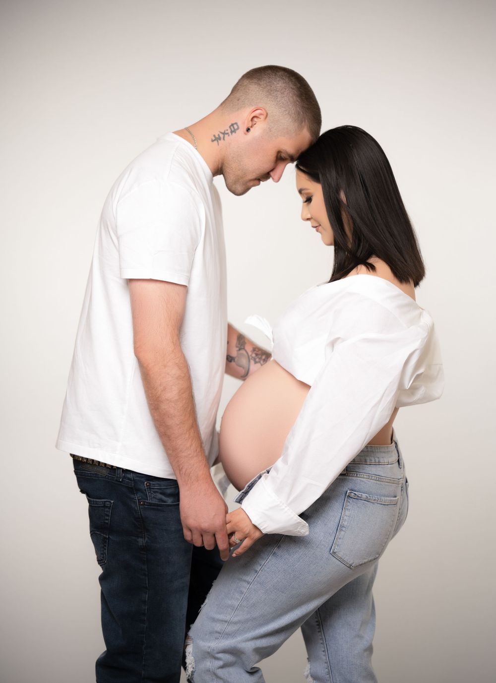 Expectant couple standing forehead to forehead during an intimate studio maternity portrait session.