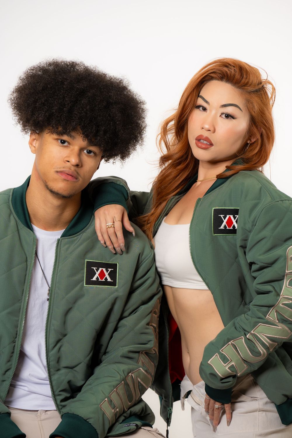 Fashion studio portrait of two models posing together in matching green jackets against a white background.