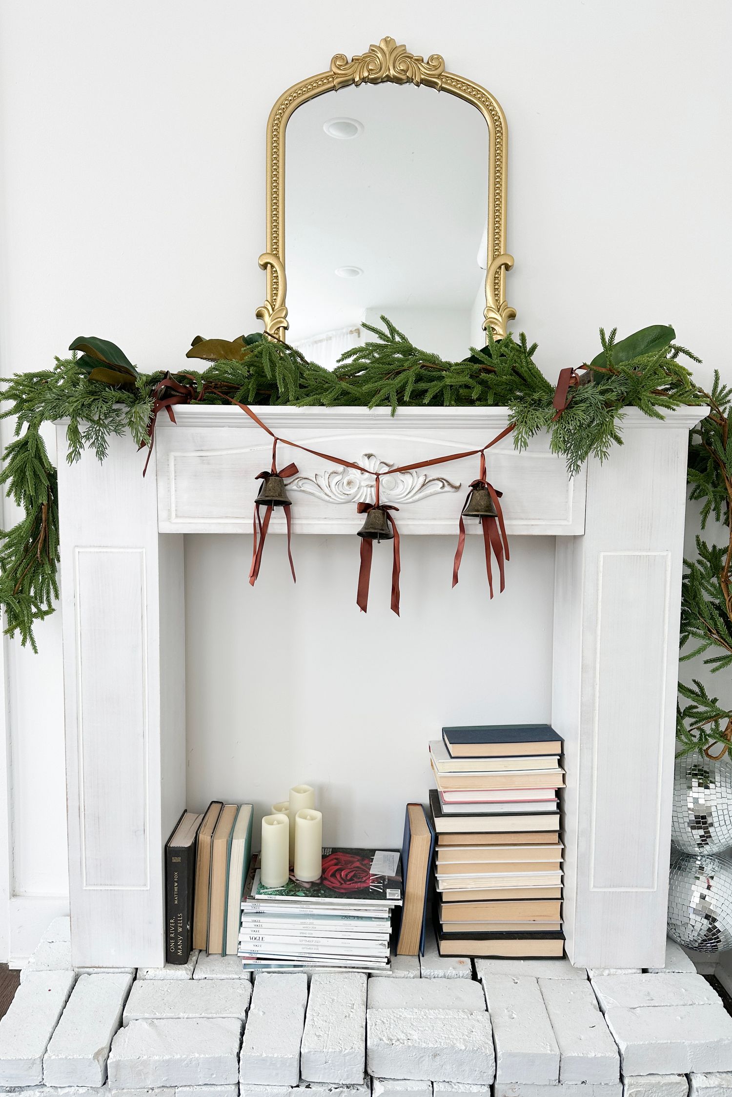 Green Norfolk pine wreath with gold velvet ribbon bow hanging on white door.
