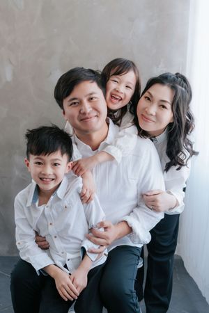 Happy Asian family of four posing together in white shirts for a professional studio portrait photo.