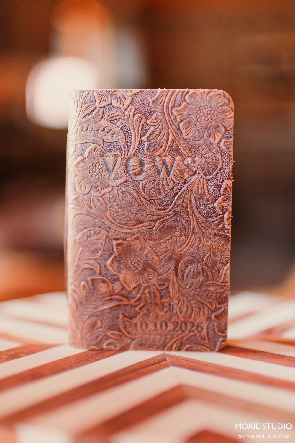 Embossed leather vows book with floral design dated 10.10.2026 on chevron surface.