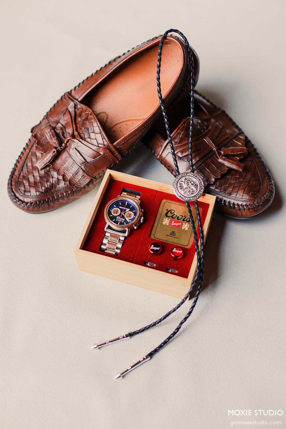 Brown woven leather loafers displayed with a wooden gift box containing a chronograph watch, cufflinks, and Coors memorabilia.