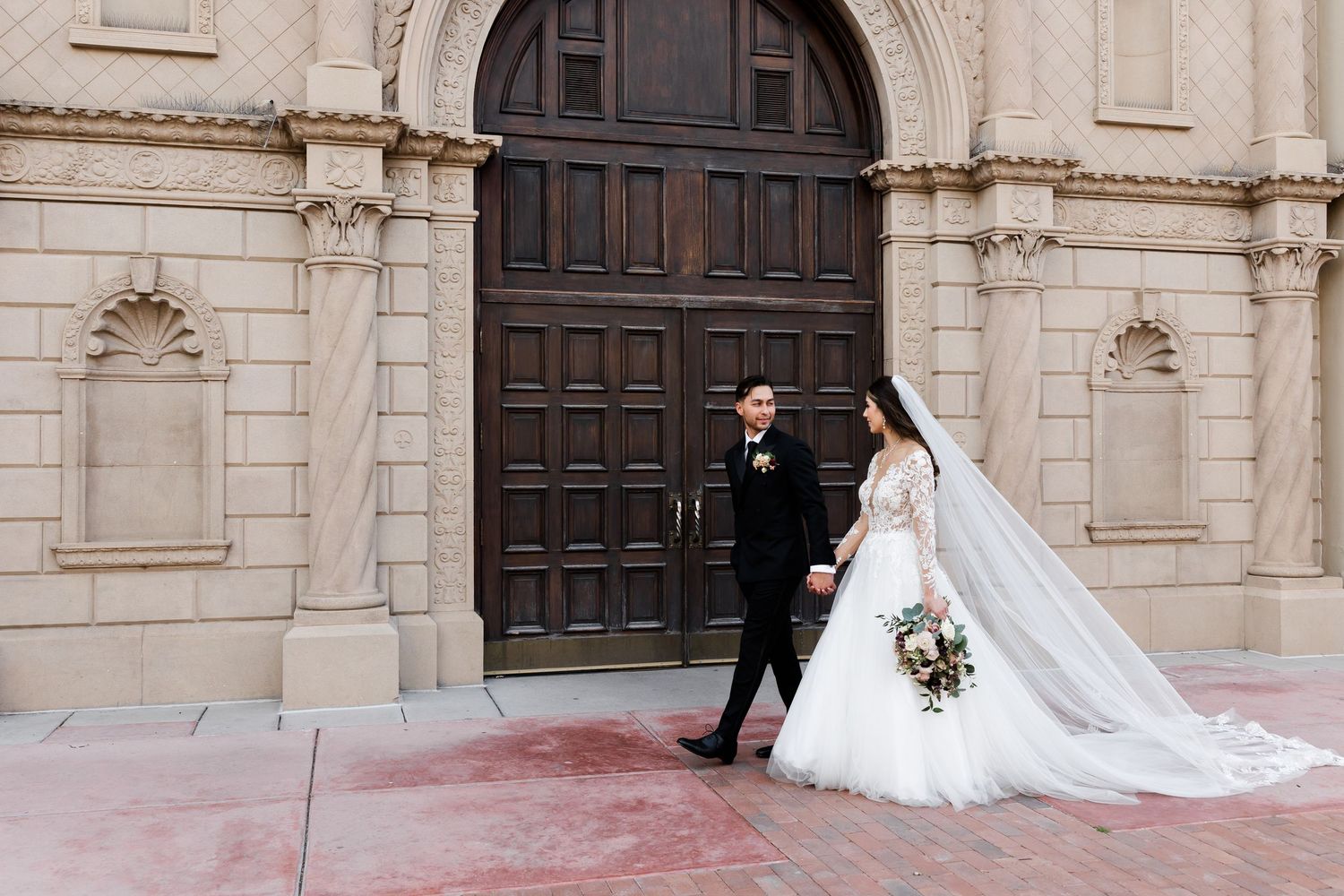 Bride and groom pose together in a lush garden courtyard with terracotta walls and greenery on their wedding day.