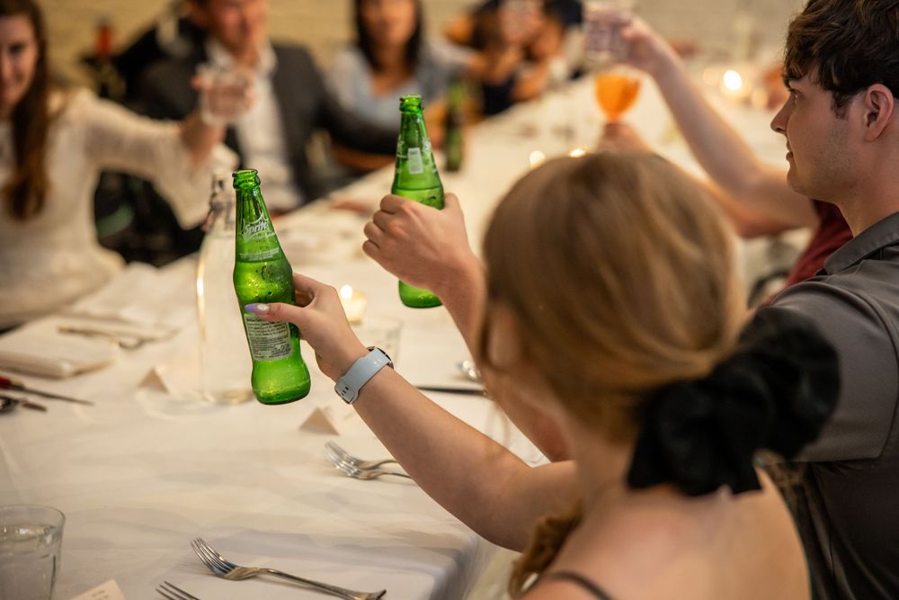 Group of people toasting with green beer bottles at a formal dinner party event.
