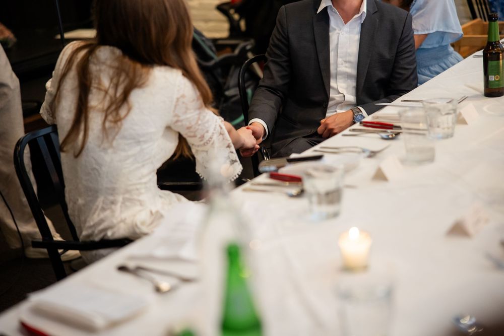 Guests seated at an elegant white tablecloth dinner table with candles and green glass bottles at a formal event.