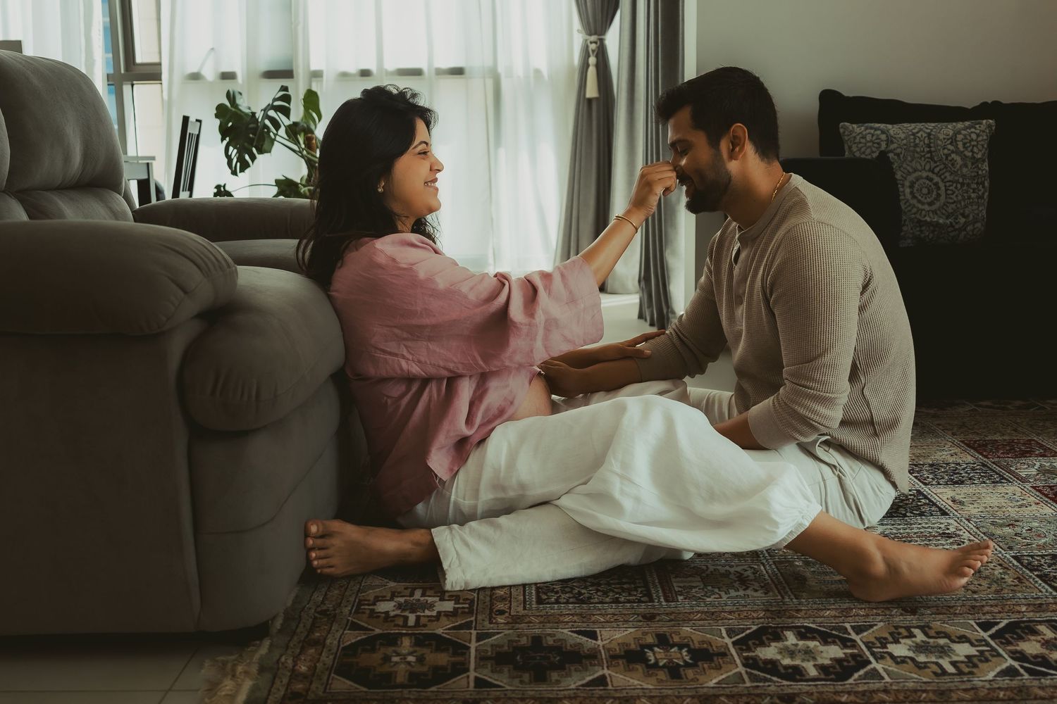 Couple sitting together on the living room floor, smiling, during an in-home maternity session in Dubai