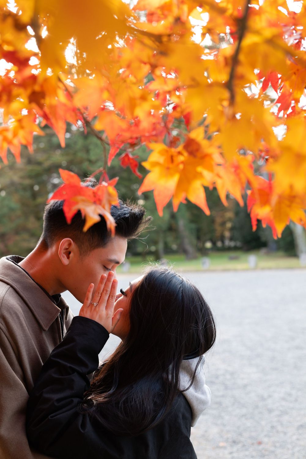Couple sharing a tender moment under vibrant orange and red autumn maple leaves in a peaceful park.