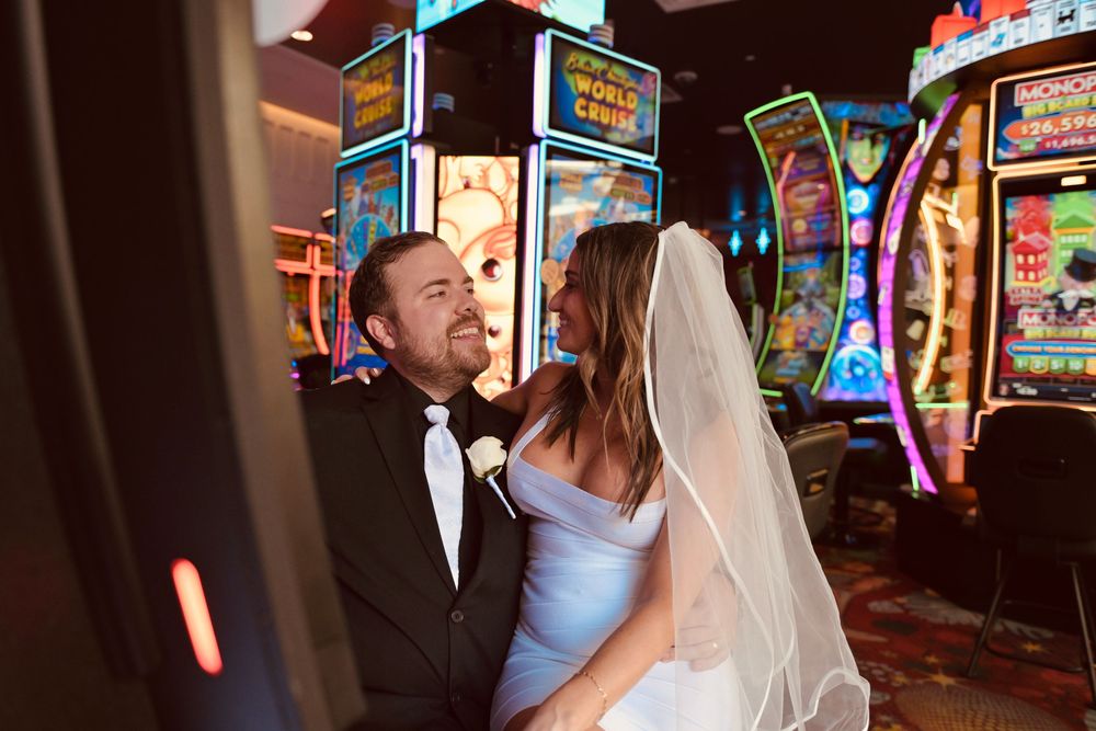 Bride in blue dress and veil with groom in tuxedo posing by slot machines in a Las Vegas casino.