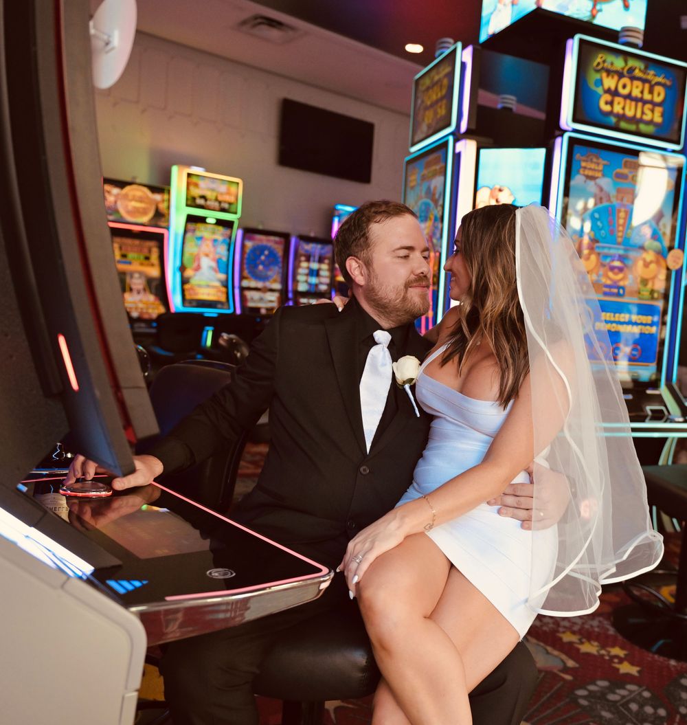 Bride and groom sharing a romantic kiss at a Las Vegas casino slot machine, bride seated on groom's lap.
