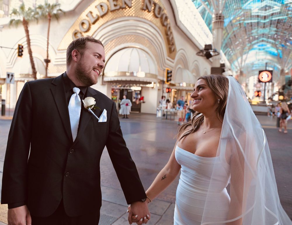 A newlywed couple holds hands and smiles at each other in wedding attire outside the Golden Nugget in Las Vegas.