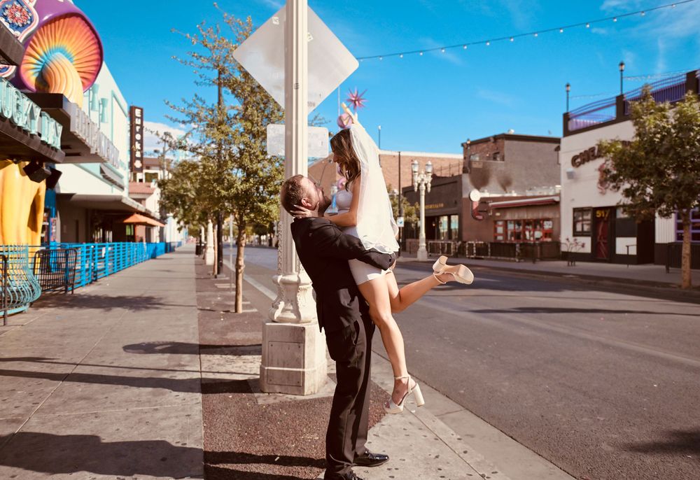 Groom lifting bride in wedding attire on a sunny urban street, celebrating their Las Vegas wedding day.