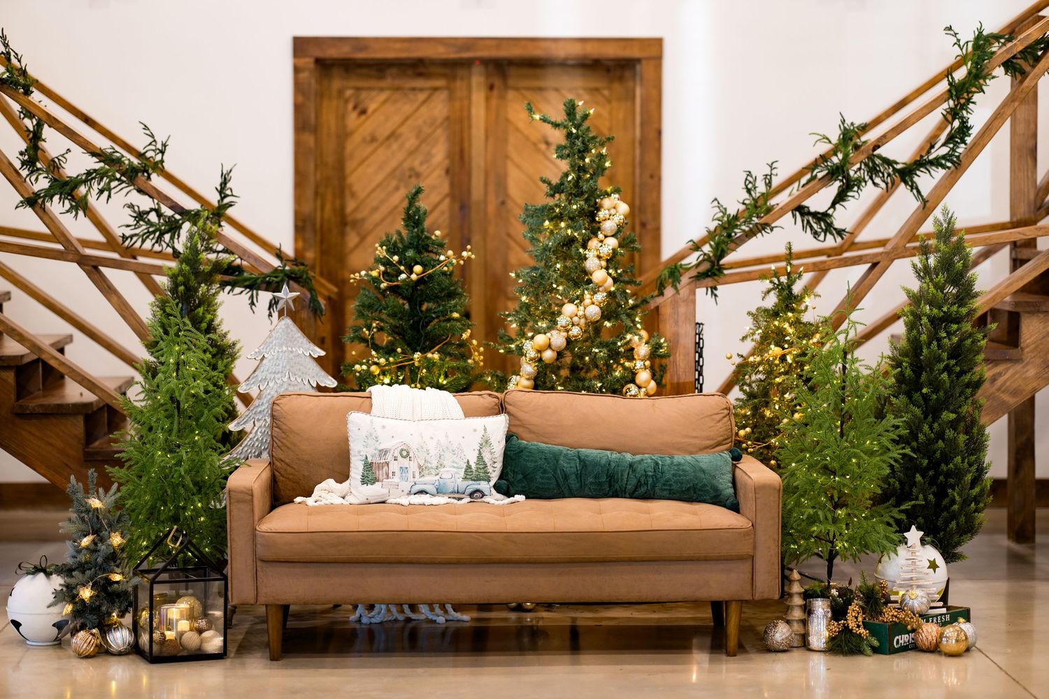 Festive holiday decor with a brown leather sofa surrounded by lit Christmas trees and garland-draped staircases.