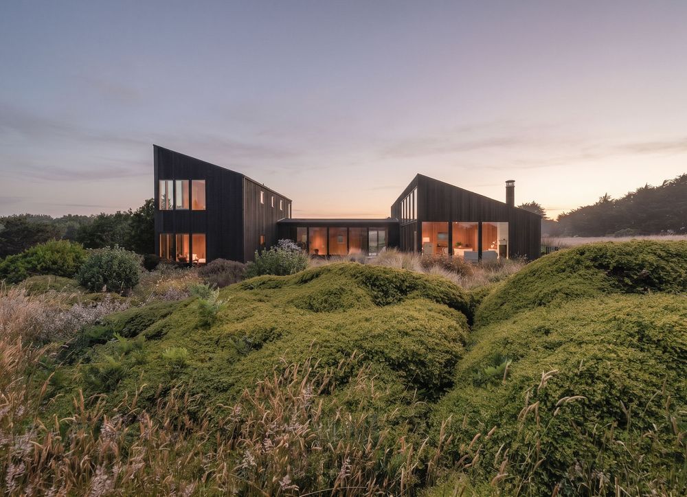 Dark modern cabin homes nestled among lush green mounds in a wild landscape at dusk.