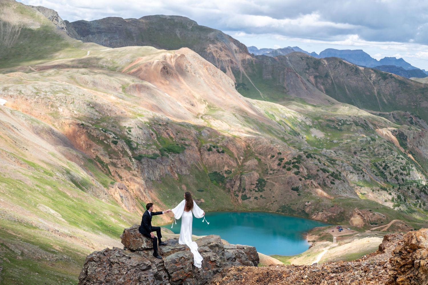 A bride and groom stand together on a mountain ridge with the snow-capped peaks of the San Juan mountains in the distance in the fall.
