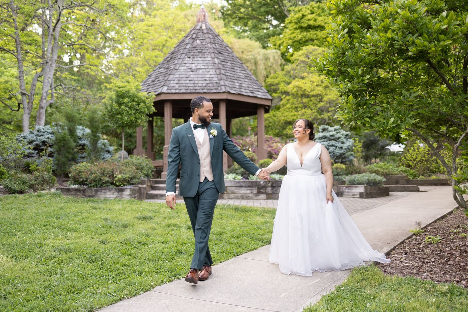 Grooms in dark suits laughing and chatting while walking together outside a brick building.
