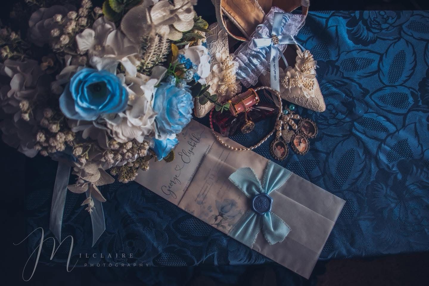 Blue floral wedding bouquet with roses beside envelope, pearl jewelry, and accessories on satin fabric. Reddit h