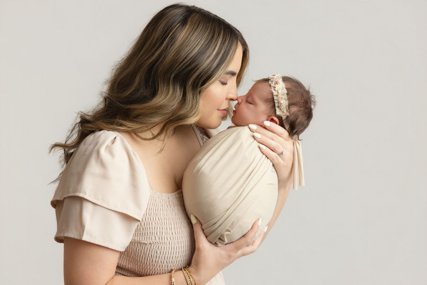 Peaceful newborn baby swaddled in cream wrap sleeping on soft beige blanket during professional newborn photography session.