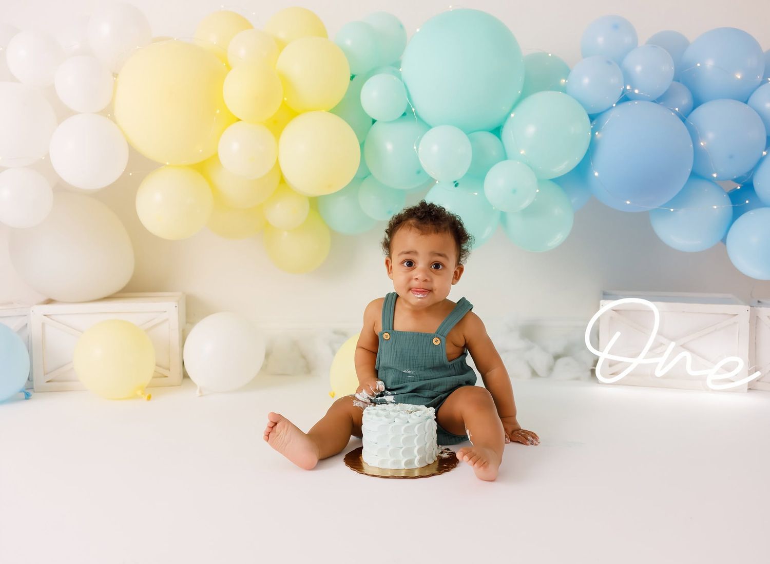 Baby's first birthday cake smash with colorful balloon arch backdrop and neon One sign.