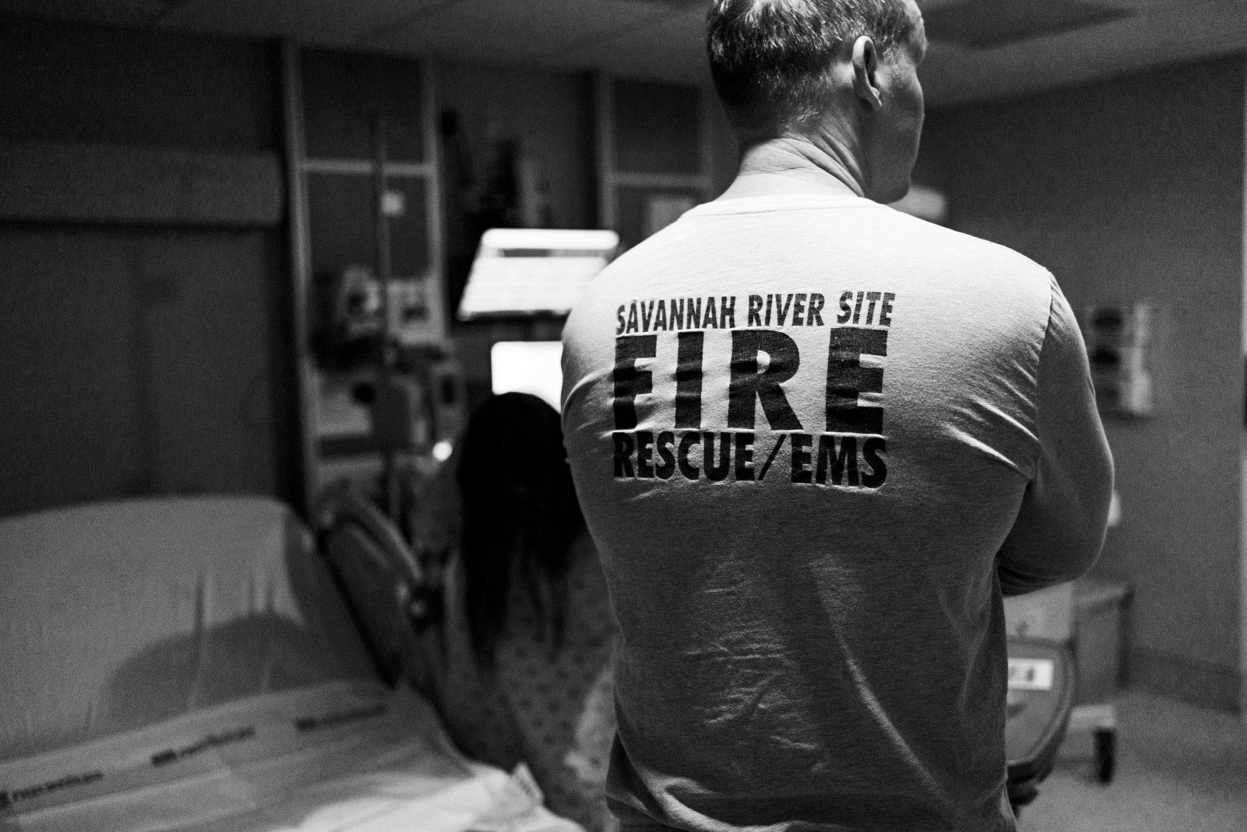 Man wearing Savannah River Site Fire Rescue EMS t-shirt standing in a room, black and white photo.