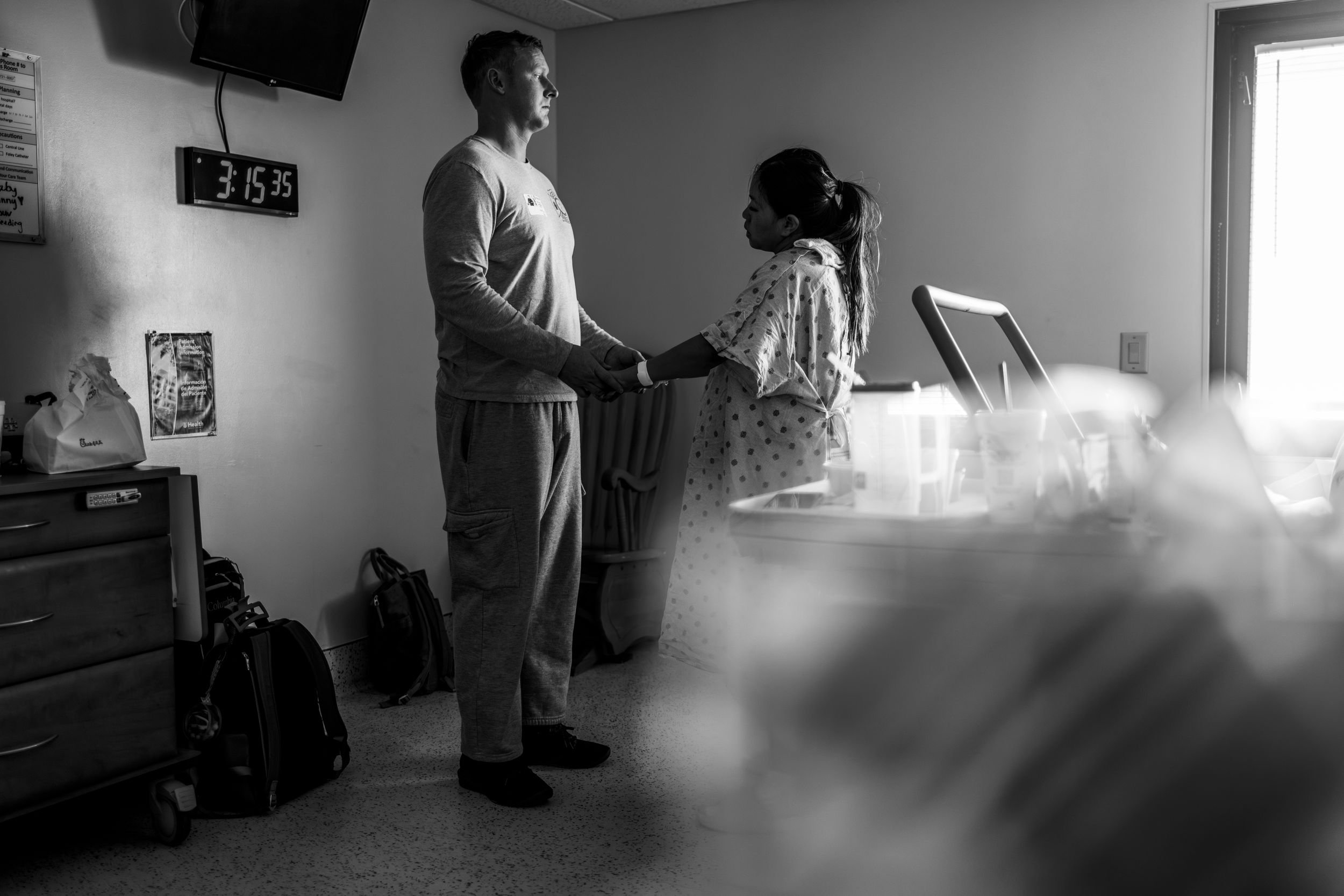 Black and white photo of a man and woman talking in a medical room with equipment and supplies visible.