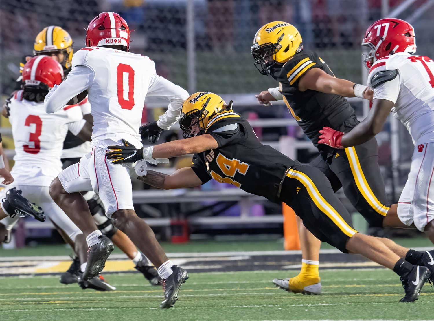 Football player in gold uniform dives to tackle opponent in red and white during an intense high school football game.