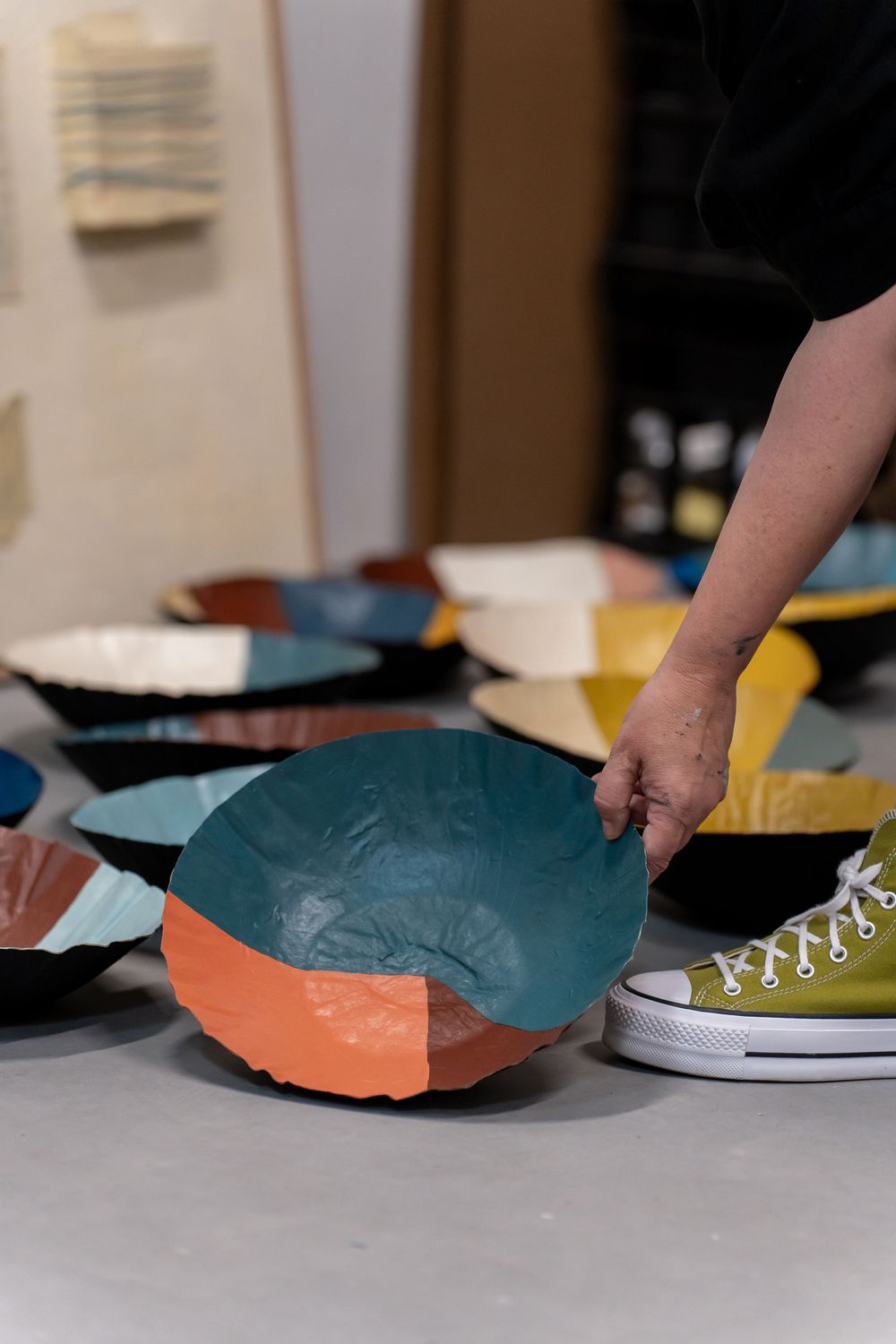 Hand holding a colorful ceramic bowl with teal and orange glaze, surrounded by multicolored pottery on a studio table.