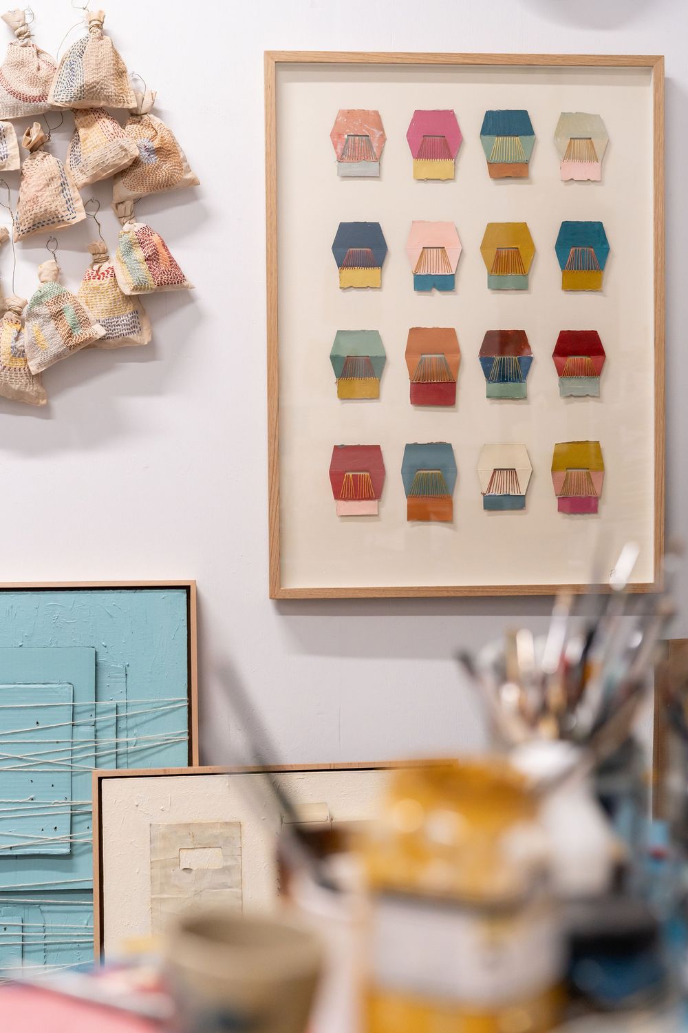 Colorful hexagonal artwork in wooden frame displayed in an artist studio with paintbrushes and framed canvases nearby.