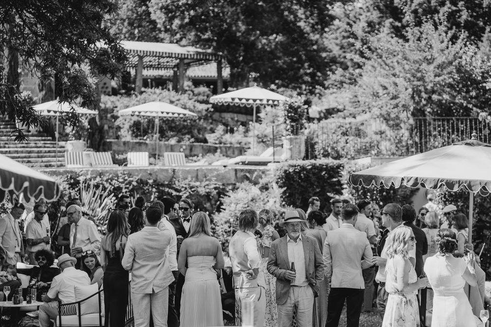 Elegant outdoor garden party with guests mingling near a gazebo surrounded by lush trees in black and white.