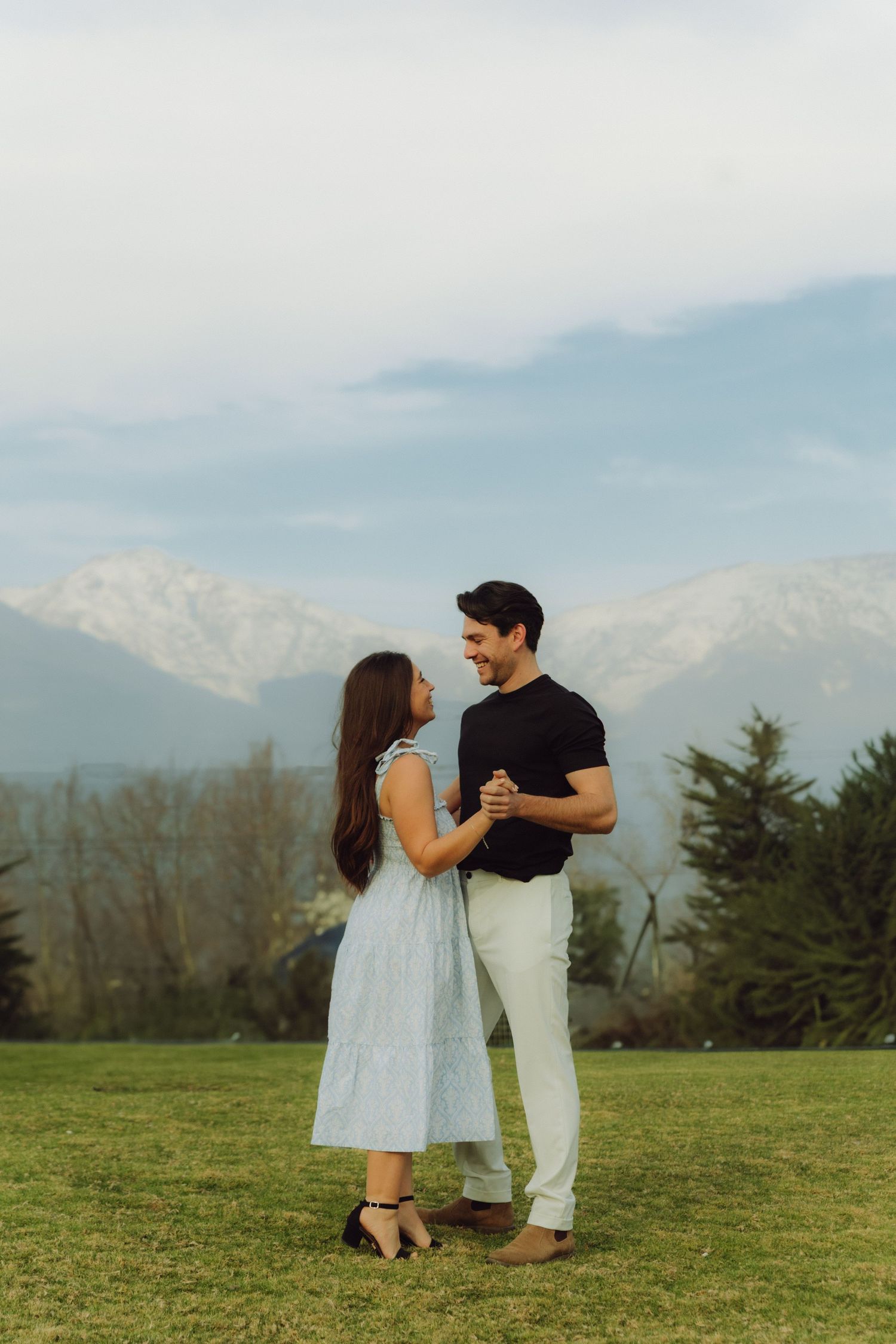 Couple dancing together on green grass with snow-capped mountains backdrop.