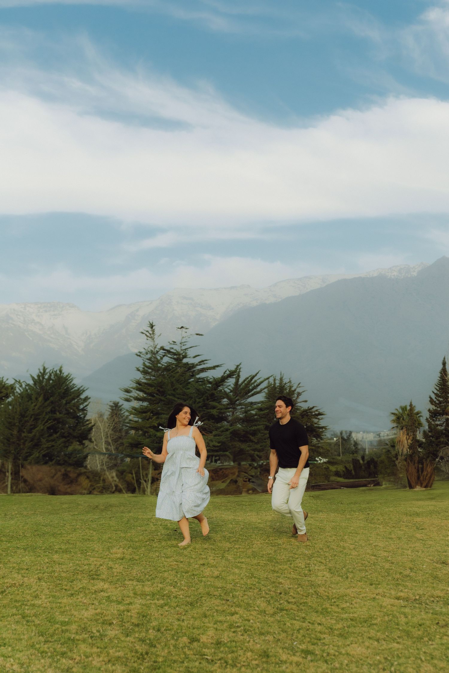 Happy couple running and laughing on green meadow with mountain views.