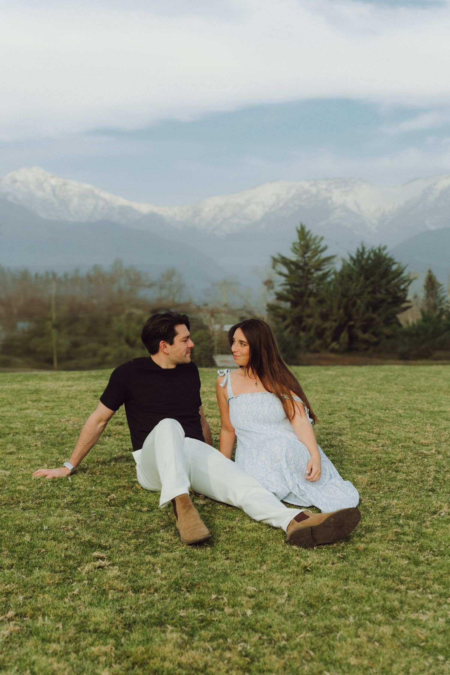 Romantic couple sitting on grass gazing at each other with snowy mountains behind.