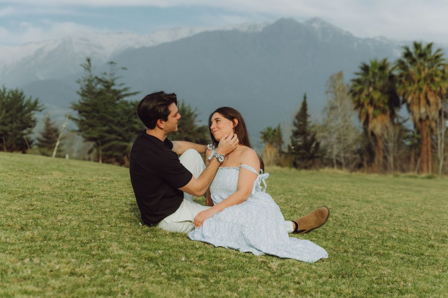 Couple sitting on lawn with palm tree and misty mountain landscape behind them.